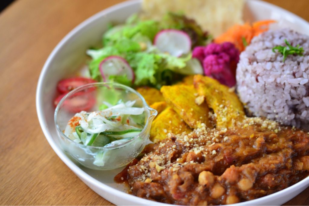 Gluten-free fresh curry made from chick peas and tomatoes, spicy chicken, rice and salad with pickles on the side.